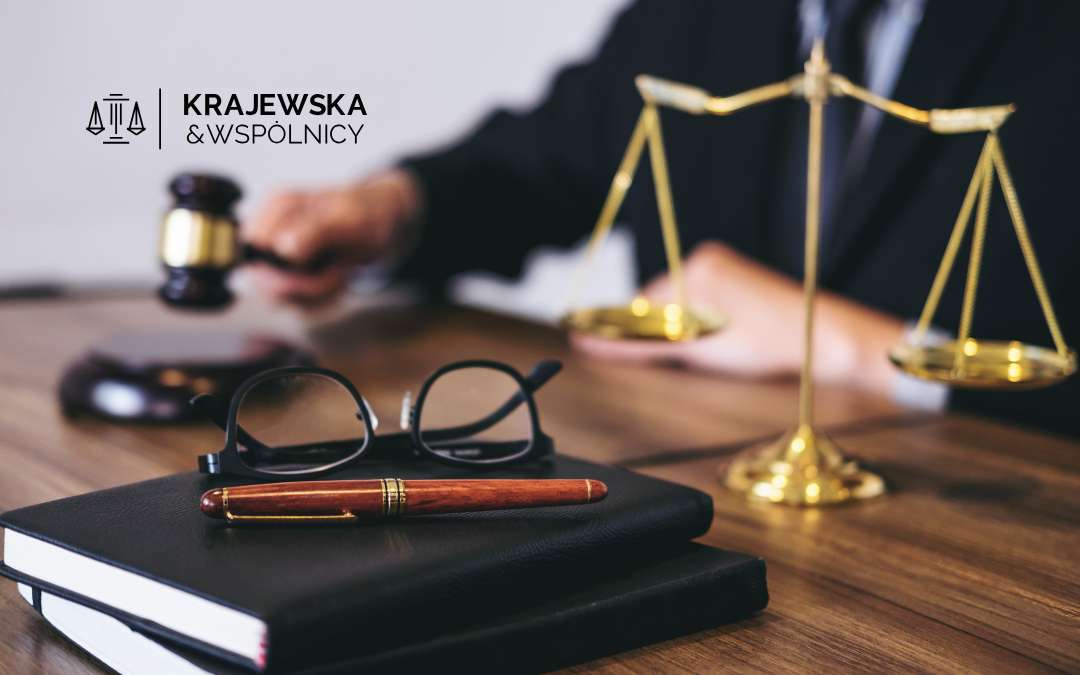 Sędzia przy biurku trzymający młotek sędziowski, na biurku złota waga, dokumenty i okulary