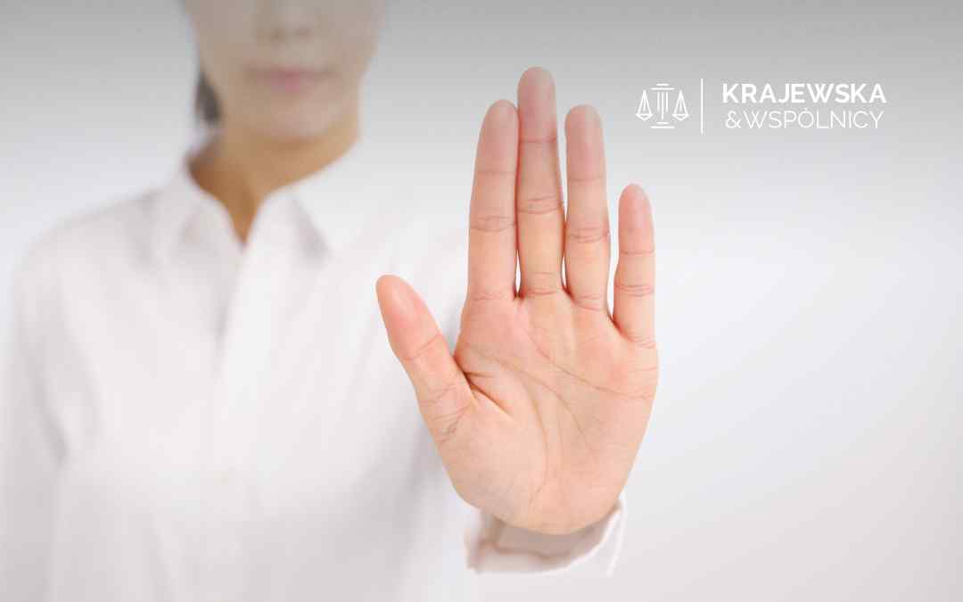 Dłoń kobiety w białej koszuli jest podniesiona w geście "stop", na jasnym tle