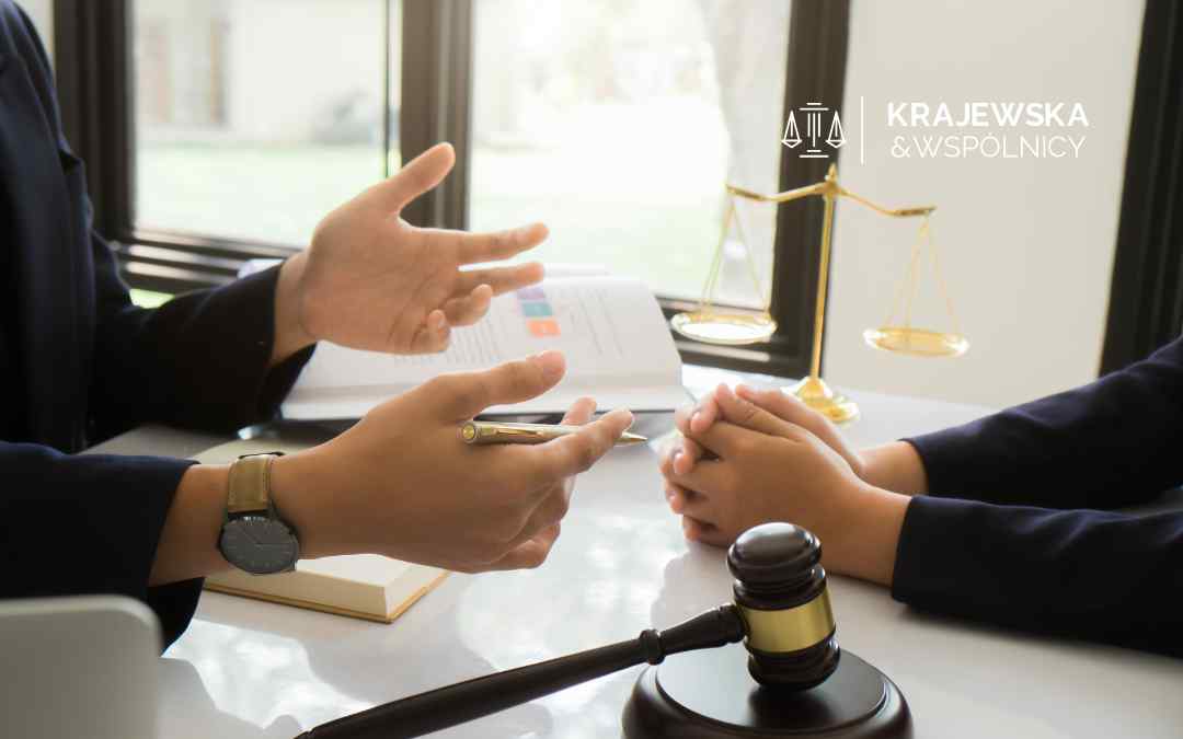 Dłoń w ciemnym garniturze trzyma dużą lupę ze złotą oprawą, powiększającą tekst na dokumencie leżącym na biurku, co symbolizuje szczegółową analizę umowy kredytowej