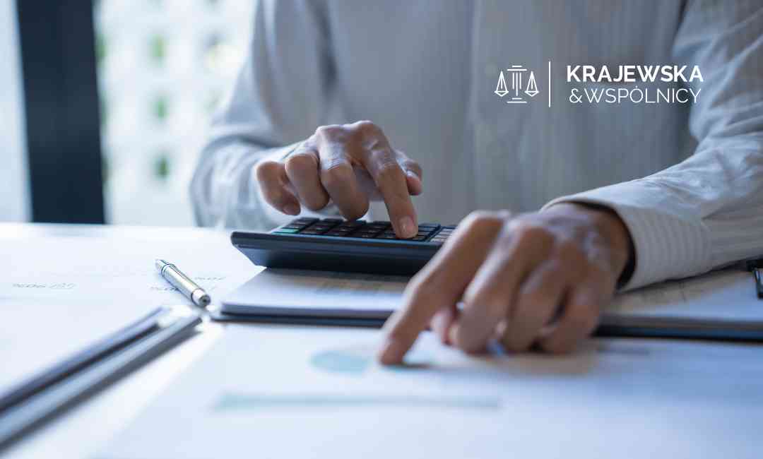 Mężczyzna wskazuje palcem dokument na stole, drugą dłonią wklepuje liczby na kalkulatorze.