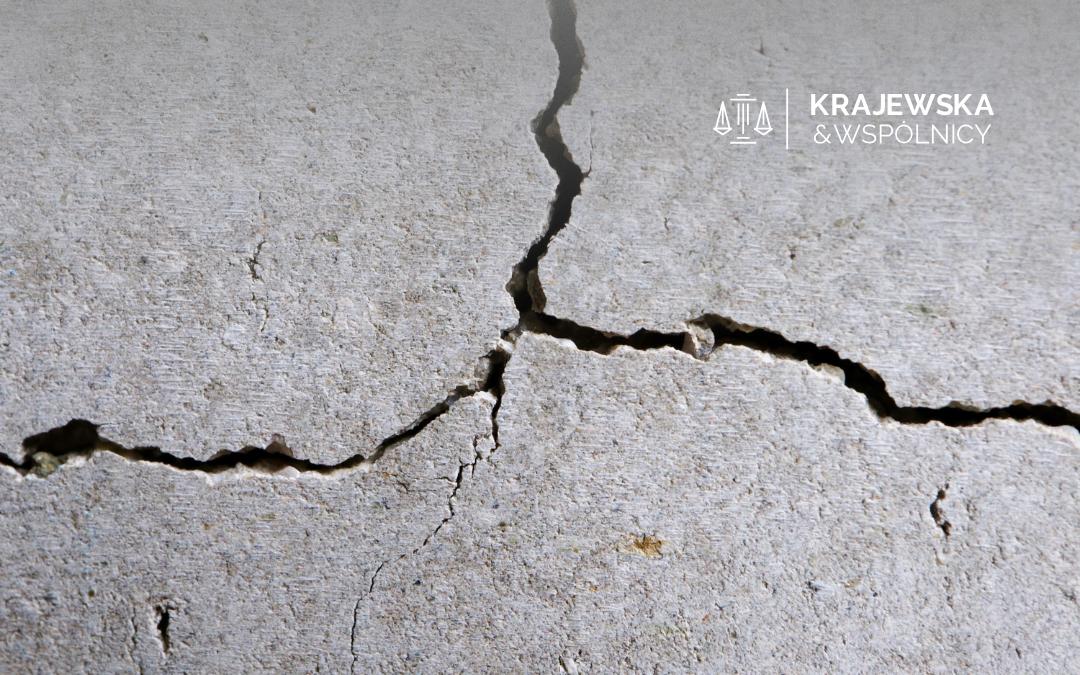 Cracked concrete surface with a large central fissure and a law firm logo in the top-right corner reading 'Krajewska & Wspólnicy'