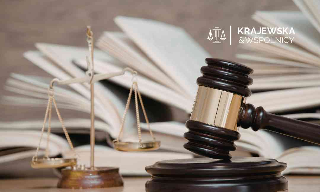 Zbliżenie na ciemny młotek sędziowski oraz mosiężną wagę szali na tle rozłożonych, otwartych ksiąg prawniczych.