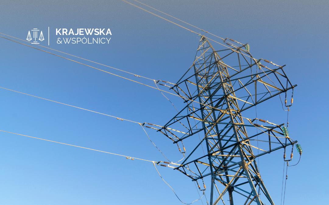 Power transmission tower and cables against a clear blue sky with the Krajewska & Wspólnicy logo in the top-left corner.