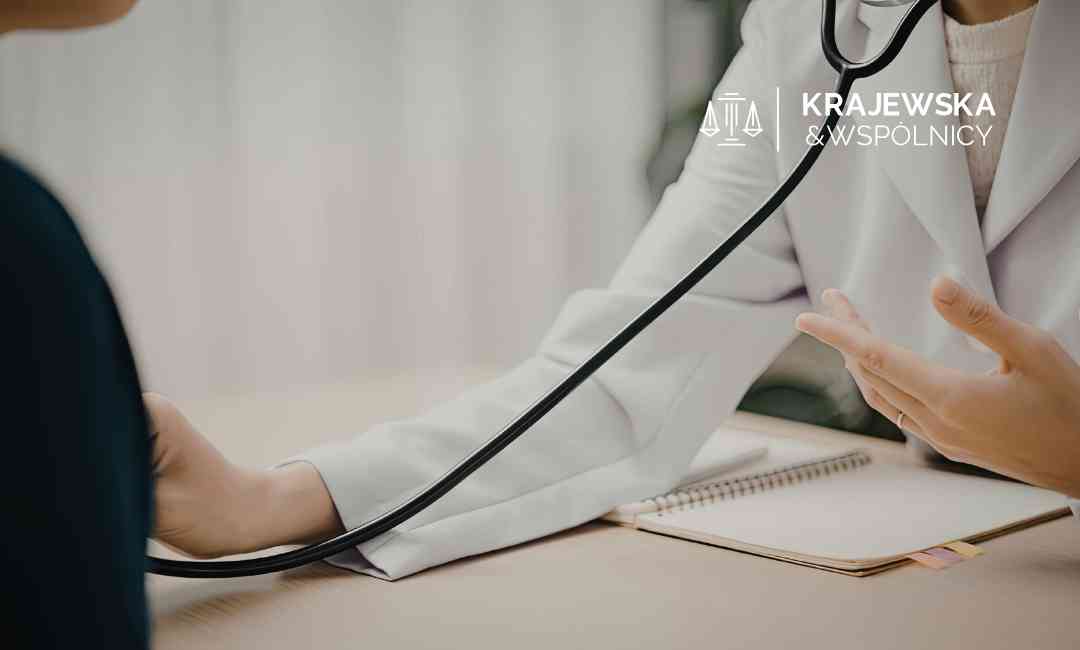 Lekarz w białym kitlu z zawieszonym na szyi stetoskopem rozmawia z pacjentem przy biurku. Lekarz gestykuluje dłonią, a przed nim leży otwarty notes.