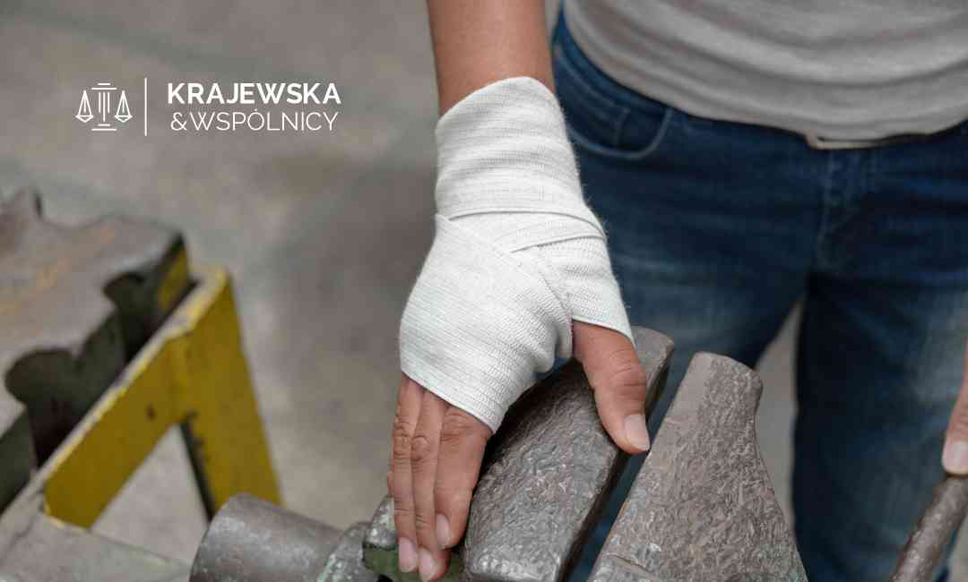 Zbliżenie na dłoń pracownika owiniętą białym bandażem medycznym podczas pracy przy imadle warsztatowym.