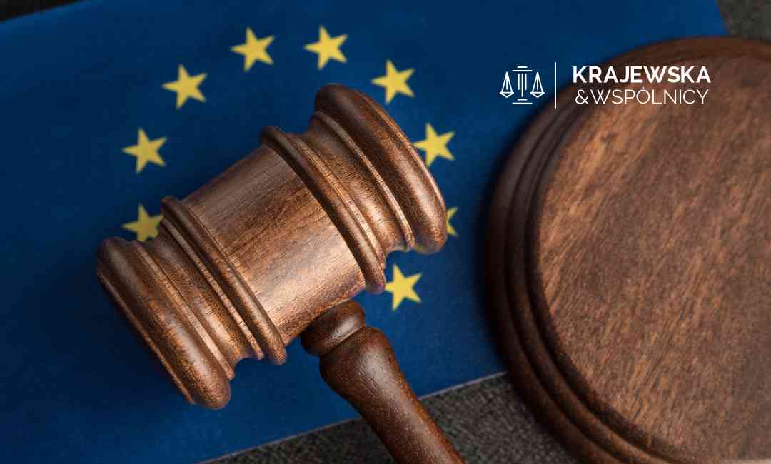 Zbliżenie na drewniany młotek sędziowski leżący na fladze Unii Europejskiej obok podstawki.