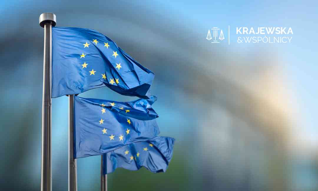 Trzy niebieskie flagi Unii Europejskiej powiewające na wietrze na tle rozmazanej, nowoczesnej architektury.