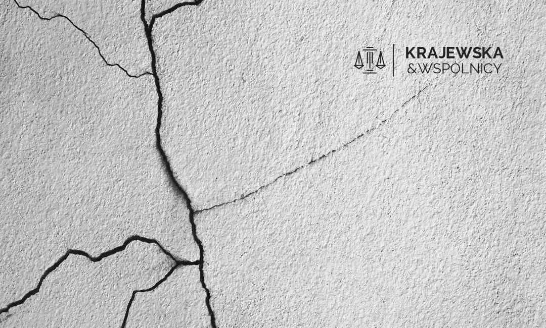 Cracked textured gray wall with the Krajewska & Wspólnicy law firm logo in the upper-right corner