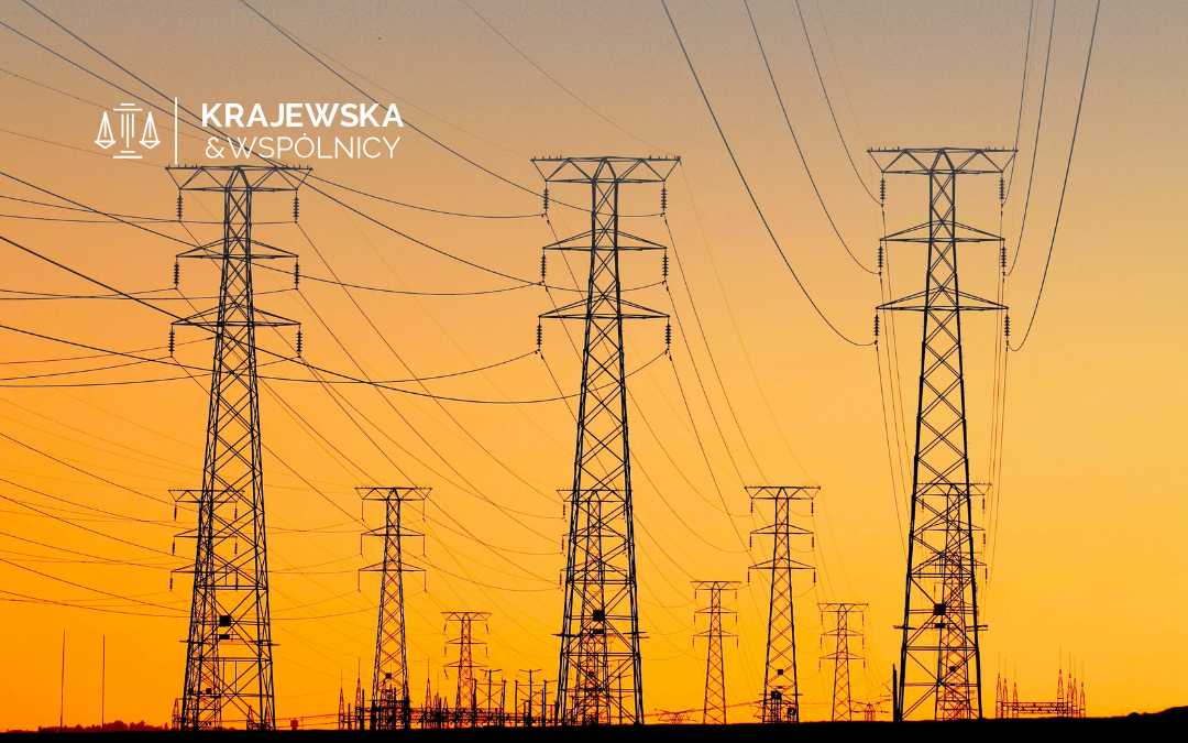 Row of steel electricity pylons and power lines silhouetted against an orange sunset, with a logo in the top-left corner.