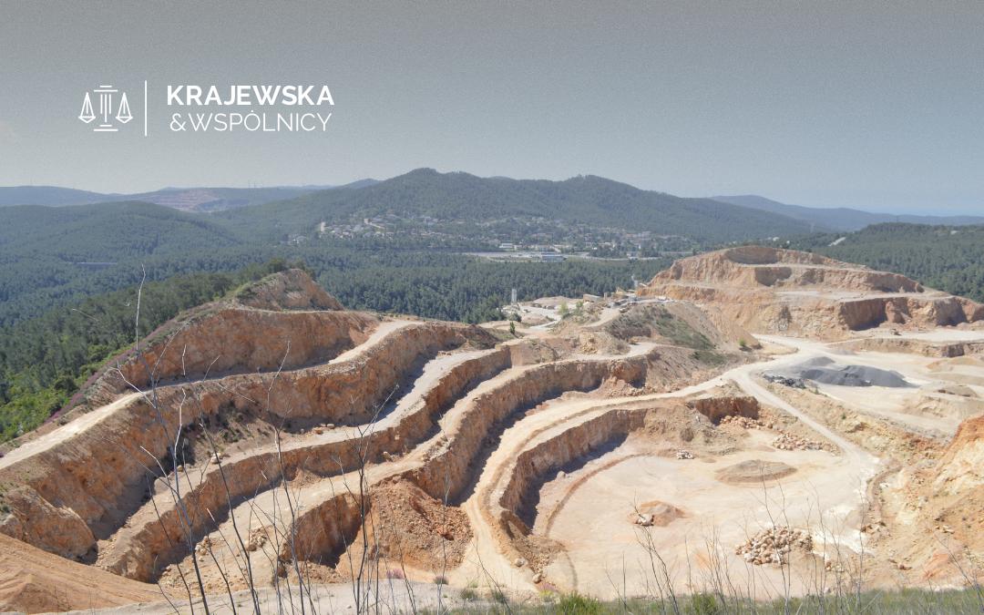 Open-pit quarry with terraced benches and distant forested hills; Krajewska & Wspólnicy logo in the top-left corner.