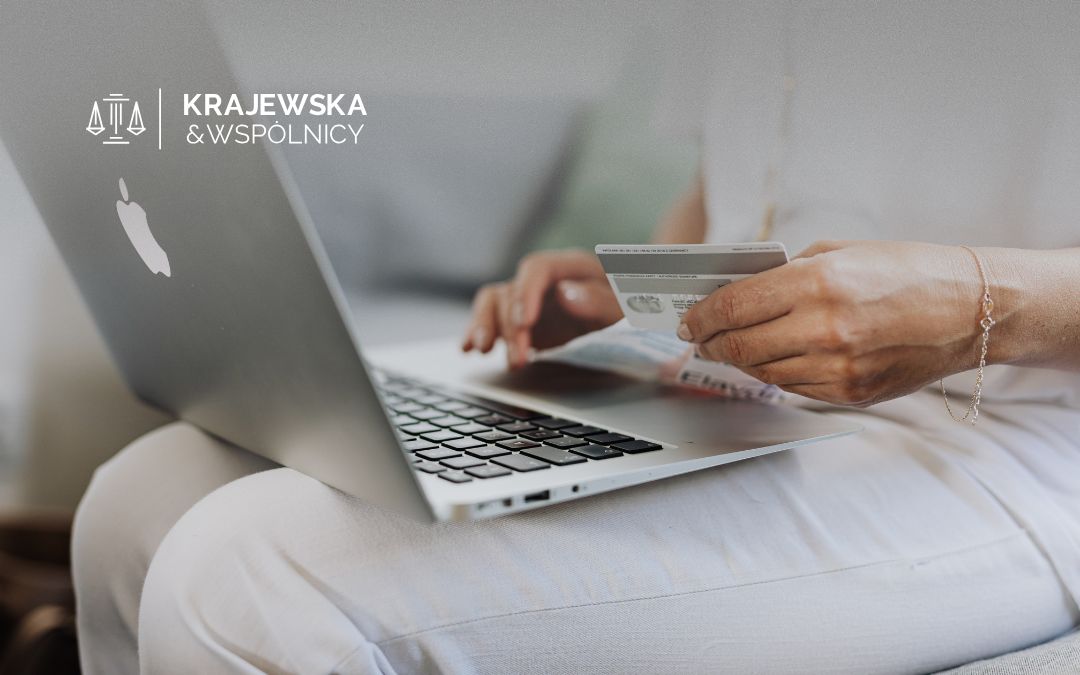 Hands hold a credit card over a silver laptop, with the Krajewska & Wspólnicy logo in the top-left corner.